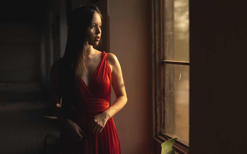 Femeie singură în rochie roșie la fereastră