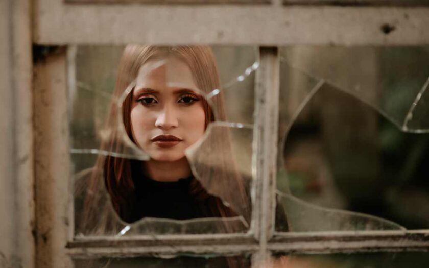 O fată privește printr-o fereastră spartă