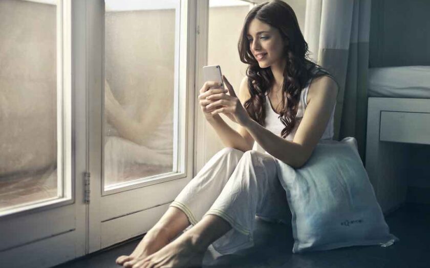 Fată în pijama stă pe telefon la fereastră